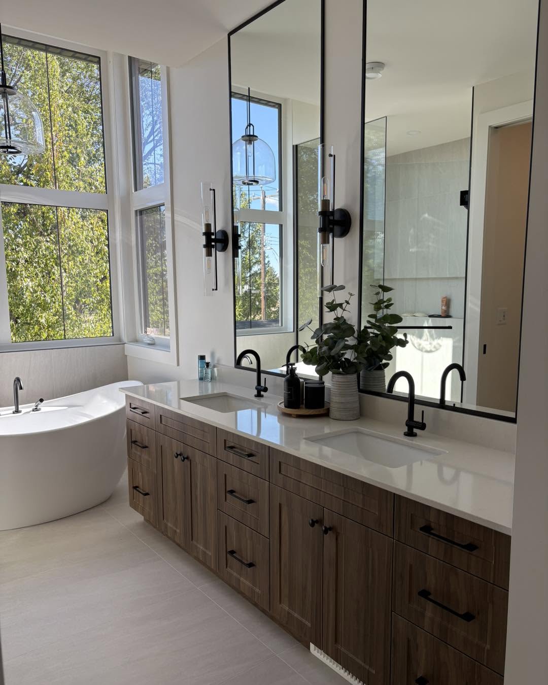 Warm wood vanity and freestanding tub by windows